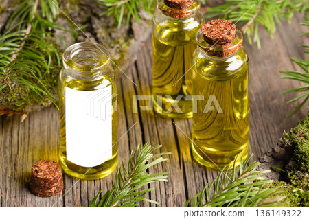 Close up essential fir oil glass bottles with cork stoppers on old wooden surface and fresh sprigs Close up essential fir oil glass bottles with cork stoppers on old wooden surface and fresh sprigs 136149322