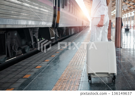 Person with luggage standing on train platform at sunrise, ready for travel adventure. Person with luggage standing on train platform at sunrise, ready for travel adventure. 136149637