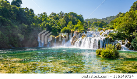 Waterfalls at Skradinski Buk, national nature park Krka, Croatia. Flowing water in beautiful nature, green plants and trees. Sunny summer day. Waterfalls at Skradinski Buk, national nature park Krka, Croatia. Flowing water in beautiful nature, green plants and trees. Sunny summer day. 136149724