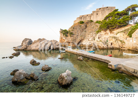 Dubrovnik old city small west harbor with boats. Near is the Lovrijenac fortress. Summer weather, morning soft light. Part of UNESCO heritage. Dubrovnik old city small west harbor with boats. Near is the Lovrijenac fortress. Summer weather, morning soft light. Part of UNESCO heritage. 136149727