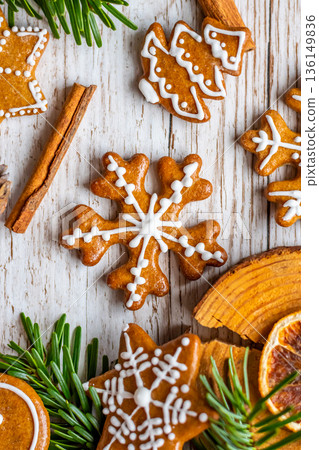 Christmas gingerbread and sweets are placed on wooden desk. Cookies and sweet food in shape of stars and snow flakes. Winter theme, rustic style. Pine trees on the side. Candy stick and other spice. 136149836