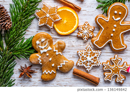 Christmas gingerbread and sweets are placed on wooden desk. Cookies and sweet food in shape of stars and snow flakes. Winter theme, rustic style. Pine trees on the side. Candy stick and other spice. 136149842