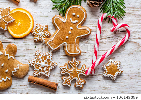 Christmas gingerbread and sweets are placed on wooden desk. Cookies and sweet food in shape of stars and snow flakes. Winter theme, rustic style. Pine trees on the side. Candy stick and other spice. Christmas gingerbread and sweets are placed on wooden desk. Cookies and sweet food in shape of stars and snow flakes. Winter theme, rustic style. Pine trees on the side. Candy stick and other spice. 136149869