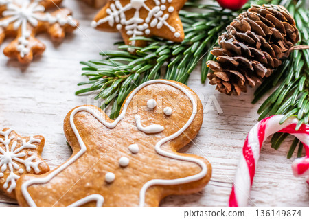 Christmas gingerbread and sweets are placed on wooden desk. Cookies and sweet food in shape of stars and snow flakes. Winter theme, rustic style. Pine trees on the side. Candy stick and other spice. 136149874