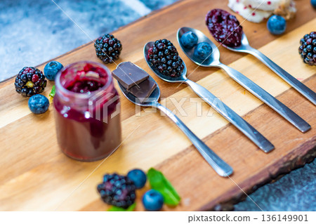 Blueberry, blackberry and chocolate are placed in silver spoon on wooden desk. Ingredients for marmalade. Fresh fruit around. 136149901