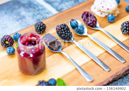 Blueberry, blackberry and chocolate are placed in silver spoon on wooden desk. Ingredients for marmalade. Fresh fruit around. 136149902