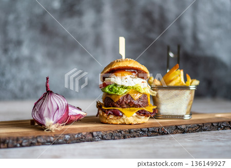 Homemade cheeseburger placed on wooden desk, with the onion and french fries on the side. Gray background. 136149927