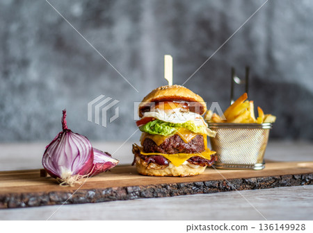 Homemade cheeseburger placed on wooden desk, with the onion and french fries on the side. Gray background. 136149928