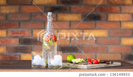 Refreshment drink with strawberry and lime placed on wooden desk. Two glasses with ice. Brick wall background. Refreshment drink with strawberry and lime placed on wooden desk. Two glasses with ice. Brick wall background. 136149933