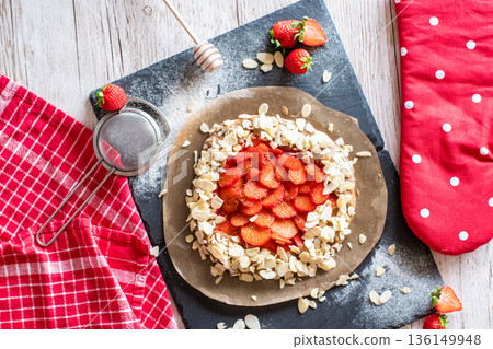 Homemade galette pie cake with strawberries and almond, placed on black desk and wooden table. Red towel with cooking tools on the side Homemade galette pie cake with strawberries and almond, placed on black desk and wooden table. Red towel with cooking tools on the side 136149948