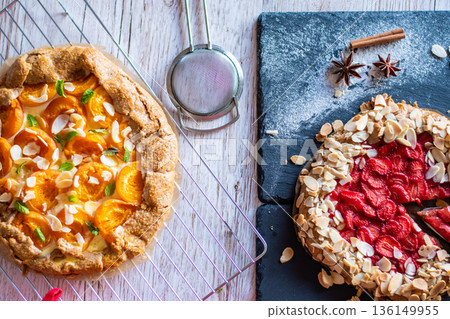 Apricot and strawberry galette placed on wooden table with cooking tools on the side. 136149955