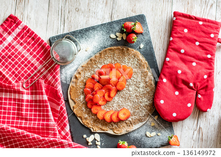 Homemade galette pie cake with strawberries and almond, placed on black desk and wooden table. Red towel with cooking tools on the side Homemade galette pie cake with strawberries and almond, placed on black desk and wooden table. Red towel with cooking tools on the side 136149972