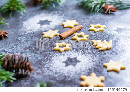 Christmas sweets and cookies in form of christmas tree placed on gray desk with pine cone and branch on the side. Winter and christmas decorations, cinnamon, sugar and star anise. 136149979