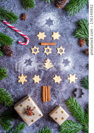Christmas sweets and cookies in form of christmas tree placed on gray desk with pine cone and branch on the side. Winter and christmas decorations, cinnamon, sugar and star anise. Christmas sweets and cookies in form of christmas tree placed on gray desk with pine cone and branch on the side. Winter and christmas decorations, cinnamon, sugar and star anise. 136149982