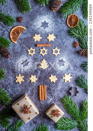 Christmas sweets and cookies in form of christmas tree placed on gray desk with pine cone and branch on the side. Winter and christmas decorations, cinnamon, sugar and star anise. Christmas sweets and cookies in form of christmas tree placed on gray desk with pine cone and branch on the side. Winter and christmas decorations, cinnamon, sugar and star anise. 136149984