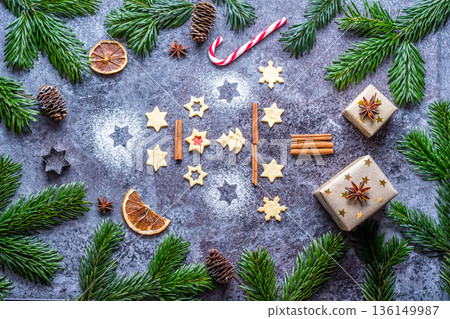 Christmas sweets and cookies in form of christmas tree placed on gray desk with pine cone and branch on the side. Winter and christmas decorations, cinnamon, sugar and star anise. 136149987