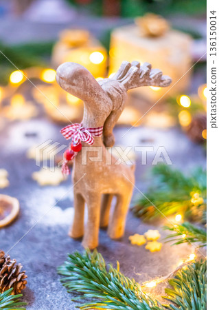 Christmas reindeer wooden toy statue with pine tree, cone and winter light in background. Christmas reindeer wooden toy statue with pine tree, cone and winter light in background. 136150014