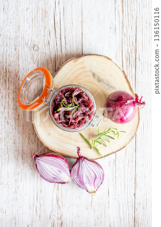 Red onion marmalade placed on wooden trunk with wood texture background. Jam from onion is delicious part of French cuisine. Homemade jam in transparent glass, vibrant colors, soft light. 136150116