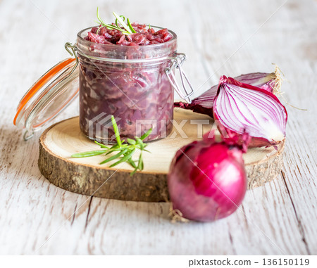 Red onion marmalade placed on wooden trunk with wood texture background. Jam from onion is delicious part of French cuisine. Homemade jam in transparent glass, vibrant colors, soft light. 136150119