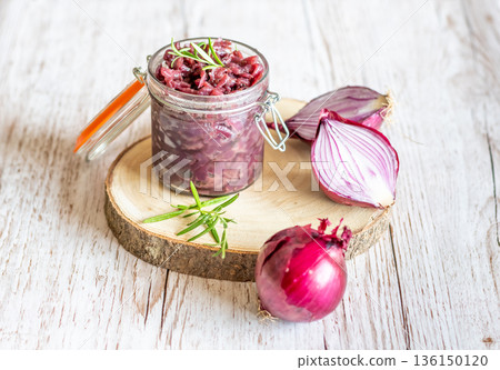Red onion marmalade placed on wooden trunk with wood texture background. Jam from onion is delicious part of French cuisine. Homemade jam in transparent glass, vibrant colors, soft light. 136150120