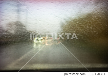 Car driving through blurred rain drops on windshield 136150311