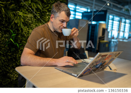 Man drinking coffee while using laptop Man drinking coffee while using laptop 136150336