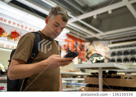 Man shopping in store browsing smartphone Man shopping in store browsing smartphone 136150339