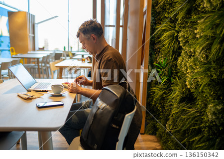 Man in cafe working on laptop Man in cafe working on laptop 136150342