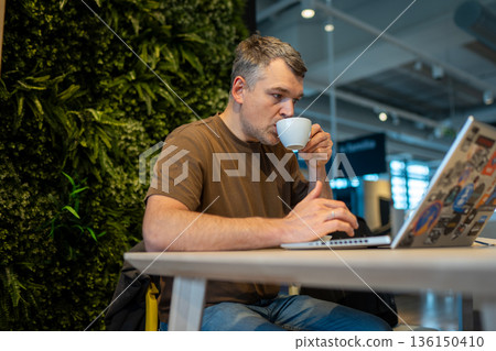 Man working at laptop while drinking coffee 136150410