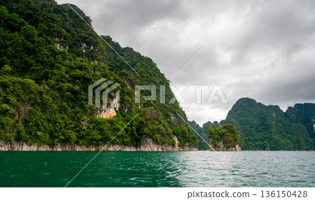 View of Khao Sok Lake in Krabi province, Thailand, with towering limestone cliffs covered in tropical rainforest rising above the calm surface of the lake. View of Khao Sok Lake in Krabi province, Thailand, with towering limestone cliffs covered in tropical rainforest rising above the calm surface of the lake. 136150428