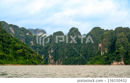 View of Khao Sok Lake in Krabi province, Thailand, with towering limestone cliffs covered in tropical rainforest rising above the calm surface of the lake. View of Khao Sok Lake in Krabi province, Thailand, with towering limestone cliffs covered in tropical rainforest rising above the calm surface of the lake. 136150432