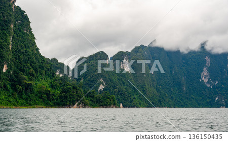 View of Khao Sok Lake in Krabi province, Thailand, with towering limestone cliffs covered in tropical rainforest rising above the calm surface of the lake. View of Khao Sok Lake in Krabi province, Thailand, with towering limestone cliffs covered in tropical rainforest rising above the calm surface of the lake. 136150435