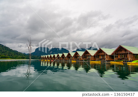 Floating wooden bungalows lined up on the calm waters of Khao Sok Lake in Thailand, surrounded by lush forests and tropical rainforest in a peaceful, remote setting. Floating wooden bungalows lined up on the calm waters of Khao Sok Lake in Thailand, surrounded by lush forests and tropical rainforest in a peaceful, remote setting. 136150437