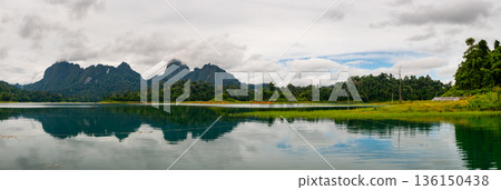 View of Khao Sok Lake in Krabi province, Thailand, with towering limestone cliffs covered in tropical rainforest rising above the calm surface of the lake. 136150438