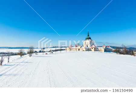 Aerial drone view of Pilgrimage Church of Saint John of Nepomuk, Zdar nad Sazavou, Czech Republic. UNESCO heritage. Ancient monastery at Zelena Hora hill. Winter weather with snow, blue sky. 136150490