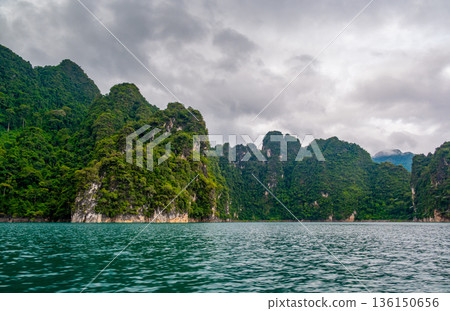 View of Khao Sok Lake in Krabi province, Thailand, with towering limestone cliffs covered in tropical rainforest rising above the calm surface of the lake. View of Khao Sok Lake in Krabi province, Thailand, with towering limestone cliffs covered in tropical rainforest rising above the calm surface of the lake. 136150656
