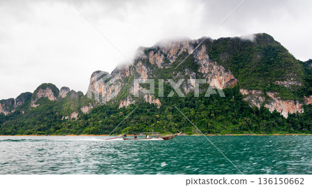 View of Khao Sok Lake in Krabi province, Thailand, with towering limestone cliffs covered in tropical rainforest rising above the calm surface of the lake. View of Khao Sok Lake in Krabi province, Thailand, with towering limestone cliffs covered in tropical rainforest rising above the calm surface of the lake. 136150662