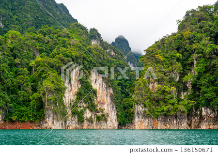 View of Khao Sok Lake in Krabi province, Thailand, with towering limestone cliffs covered in tropical rainforest rising above the calm surface of the lake. View of Khao Sok Lake in Krabi province, Thailand, with towering limestone cliffs covered in tropical rainforest rising above the calm surface of the lake. 136150671