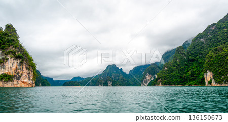 View of Khao Sok Lake in Krabi province, Thailand, with towering limestone cliffs covered in tropical rainforest rising above the calm surface of the lake. View of Khao Sok Lake in Krabi province, Thailand, with towering limestone cliffs covered in tropical rainforest rising above the calm surface of the lake. 136150673