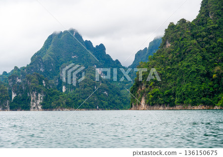 View of Khao Sok Lake in Krabi province, Thailand, with towering limestone cliffs covered in tropical rainforest rising above the calm surface of the lake. View of Khao Sok Lake in Krabi province, Thailand, with towering limestone cliffs covered in tropical rainforest rising above the calm surface of the lake. 136150675