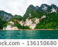 View of Khao Sok Lake in Krabi province, Thailand, with towering limestone cliffs covered in tropical rainforest rising above the calm surface of the lake. 136150680
