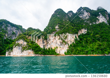 View of Khao Sok Lake in Krabi province, Thailand, with towering limestone cliffs covered in tropical rainforest rising above the calm surface of the lake. View of Khao Sok Lake in Krabi province, Thailand, with towering limestone cliffs covered in tropical rainforest rising above the calm surface of the lake. 136150680