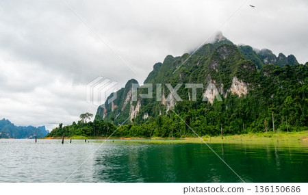 View of Khao Sok Lake in Krabi province, Thailand, with towering limestone cliffs covered in tropical rainforest rising above the calm surface of the lake. View of Khao Sok Lake in Krabi province, Thailand, with towering limestone cliffs covered in tropical rainforest rising above the calm surface of the lake. 136150686