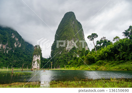 View of Khao Sok Lake in Krabi province, Thailand, with towering limestone cliffs covered in tropical rainforest rising above the calm surface of the lake. View of Khao Sok Lake in Krabi province, Thailand, with towering limestone cliffs covered in tropical rainforest rising above the calm surface of the lake. 136150690