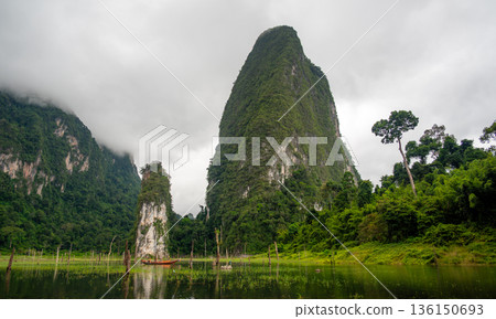View of Khao Sok Lake in Krabi province, Thailand, with towering limestone cliffs covered in tropical rainforest rising above the calm surface of the lake. View of Khao Sok Lake in Krabi province, Thailand, with towering limestone cliffs covered in tropical rainforest rising above the calm surface of the lake. 136150693