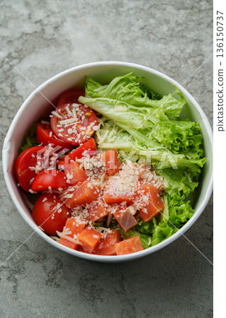 Fresh salad bowl with lettuce, tomatoes, and cheese on gray surface 136150737