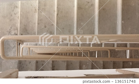 A striking perspective shot of a stairwell featuring concrete steps and a metal railing. The image conveys depth and architectural beauty, ideal for design-related projects. 136151748