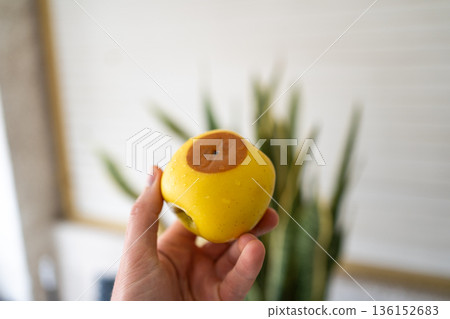 Close-up of a hand holding a yellow apple with a large brown spot, concept of rotten fruit, damaged apple, unhealthy food, organic imperfection, food waste and natural defects. Close-up of a hand holding a yellow apple with a large brown spot, concept of rotten fruit, damaged apple, unhealthy food, organic imperfection, food waste and natural defects. 136152683