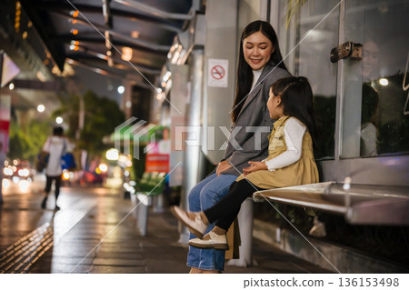 mother and child girl waiting for bus at bus stop in Bangkok city street at night, Thailand 136153498