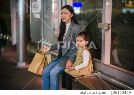 mother and child girl waiting for bus at bus stop in Bangkok city street at night, Thailand 136153499